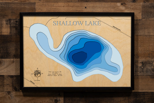 A meticulously detailed, laser-cut, multi-layered wooden topographical map of Shallow Lake in Otter Tail County, Minnesota, showcasing the intimate 65-acre surface with depth contours from shallower areas to the 28-foot maximum depth. The natural wood top layer frames 1.6 miles of shoreline in the county with more lakes than anywhere in America, while graduated blue layers create a gentle visual depth gradient.
