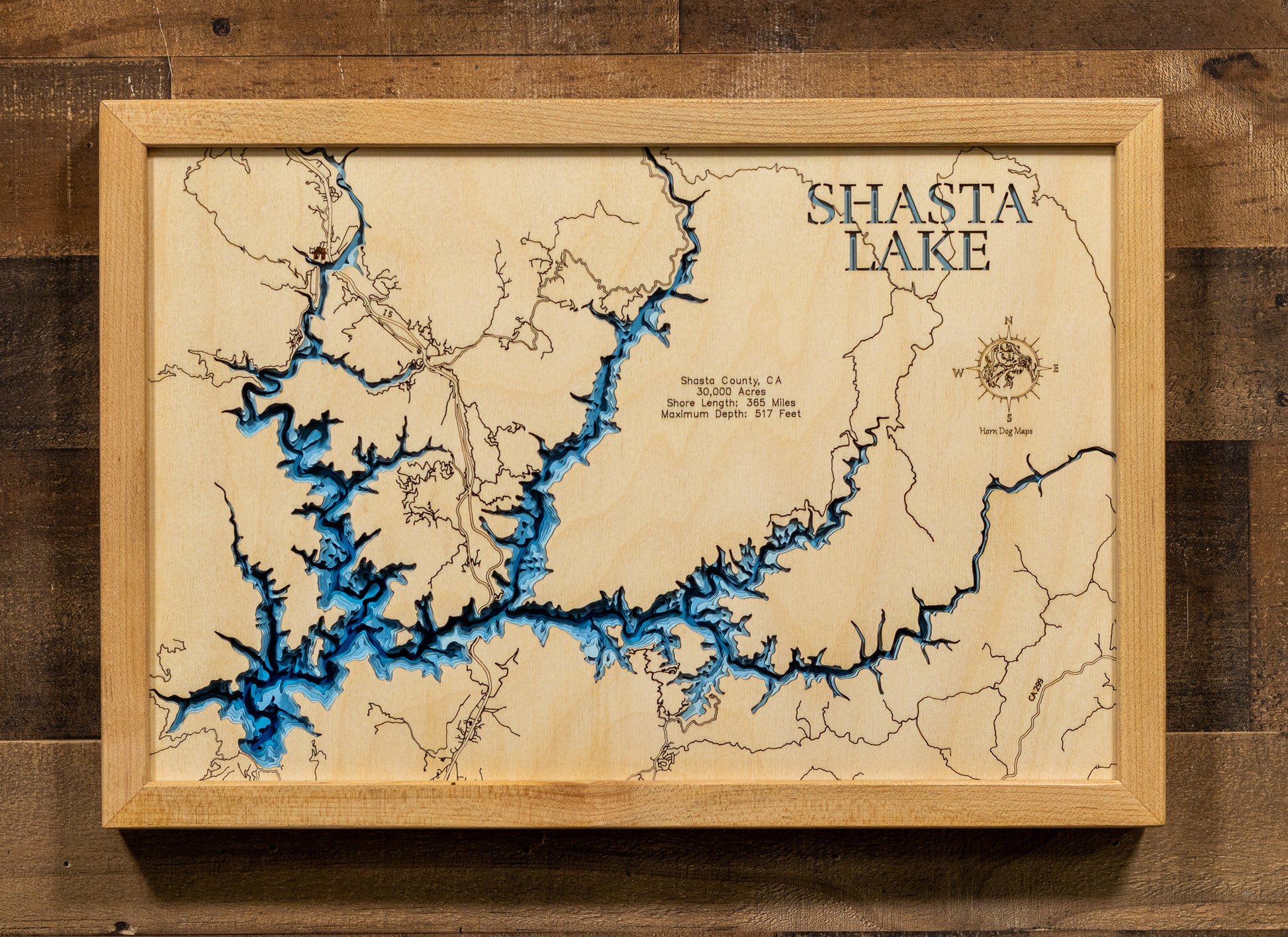 A laser-cut, layered wood map of Lake Shasta, California, showcasing its intricate shoreline and surrounding mountain terrain.