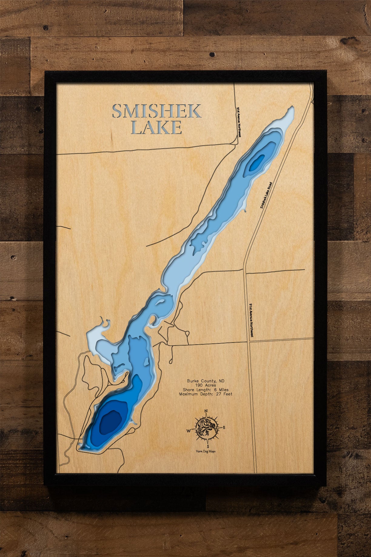 A precision laser-cut, multi-layered wooden map of Smishek Lake in Burke County, North Dakota, a 190-acre reservoir near Powers Lake known as one of northwest North Dakota's best-kept fishing secrets. The natural wood top layer captures 6 miles of rolling prairie shoreline in fine detail, while a light-to-dark blue gradient conveys the lake's 27-foot depth. A handcrafted statement piece for any North Dakota lake home, cabin, or outdoor enthusiast's wall.
