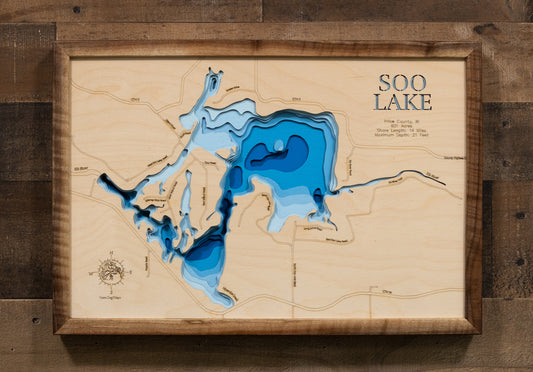 A laser-cut, layered wooden map of Lac Sault Dore (Soo Lake) in Price County, Wisconsin. The distinct irregular shape of this impoundment, with its numerous islands and 14-mile shoreline, is clearly visible within the forested landscape of northern Wisconsin. The varying depths of the lake, reaching a maximum of 21 feet, are represented by different layers of wood, illustrating its impressive underwater topography.