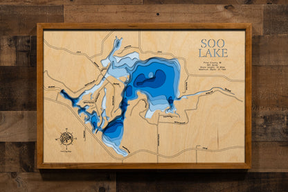 A laser-cut, layered wooden map of Lac Sault Dore (Soo Lake) in Price County, Wisconsin. The distinct irregular shape of this impoundment, with its numerous islands and 14-mile shoreline, is clearly visible within the forested landscape of northern Wisconsin. The varying depths of the lake, reaching a maximum of 21 feet, are represented by different layers of wood, illustrating its impressive underwater topography.