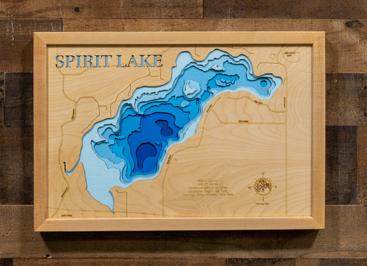 A framed wooden depth map of Spirit Lake, featuring layered blue and light blue water contours on a light wood grain background, mounted on a dark wood plank wall.