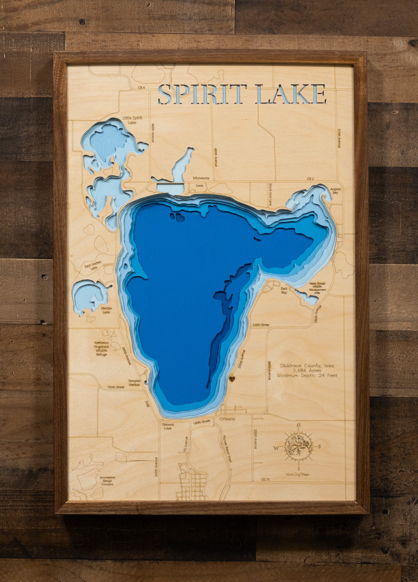 A laser-cut, layered wooden map of Spirit Lake in Dickinson County, Iowa. The relatively circular shape of Iowa's largest natural lake is clearly visible within the northwestern Iowa landscape. The varying depths of the lake, reaching a maximum of 24 feet, are represented by different layers of wood.