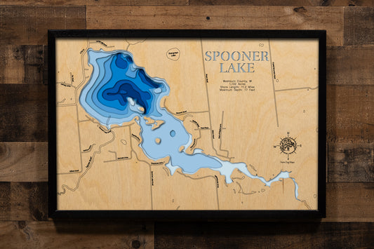 A precision laser-cut, multi-layered wooden map of Spooner Lake in Washburn County, Wisconsin. The natural wood top layer traces the lake's 11.2 miles of shoreline, five islands, and expansive bays in fine detail, while a light-to-dark blue gradient highlights the water's depth and dimension. A distinctive, rustic statement piece crafted for cabin walls, lake homes, or any Wisconsin Northwoods-inspired living space.