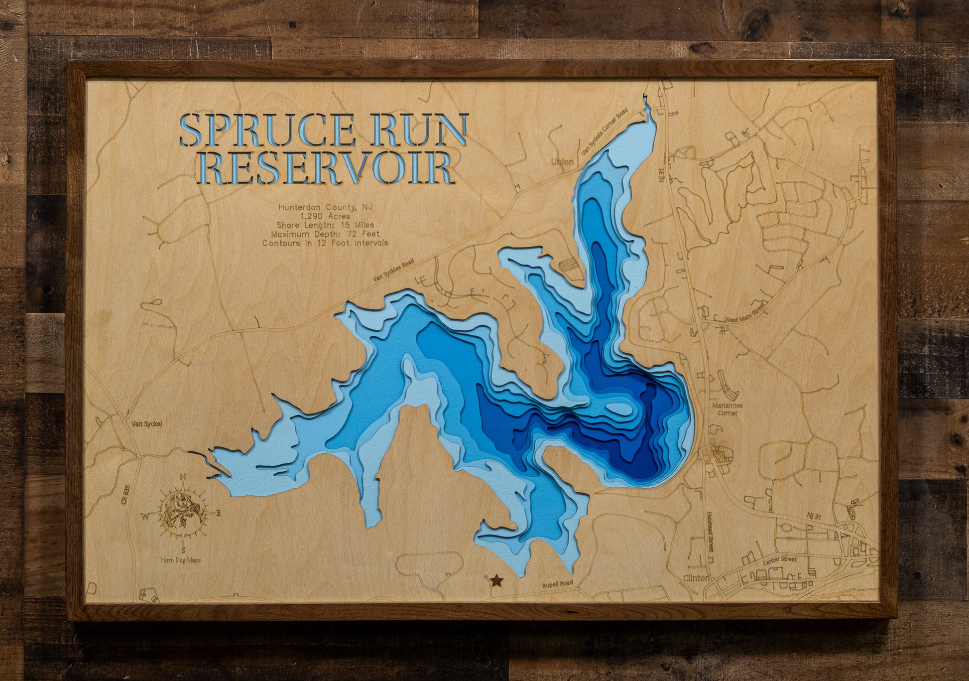 A laser-cut, layered wooden map of Spruce Run Reservoir in Hunterdon County, New Jersey. The distinct shape of this large reservoir, with its 15-mile shoreline, is clearly visible within the central New Jersey landscape. The varying depths of the lake, now confirmed to reach a maximum of 72 feet and detailed by 12-foot contour intervals, are represented by different layers of wood, illustrating its impressive underwater topography.