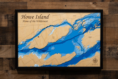 A precision laser-cut, multi-layered wooden map of Howe Island on the St. Lawrence River, centered on the second-largest of the Thousand Islands spanning the Ontario and New York border. The natural wood top layer captures the island's dramatic 8-mile form amid the surrounding river channels, while a light-to-dark blue gradient conveys depths reaching 250 feet. A stunning handcrafted piece for any Thousand Islands home, cottage, or waterway enthusiast's wall.