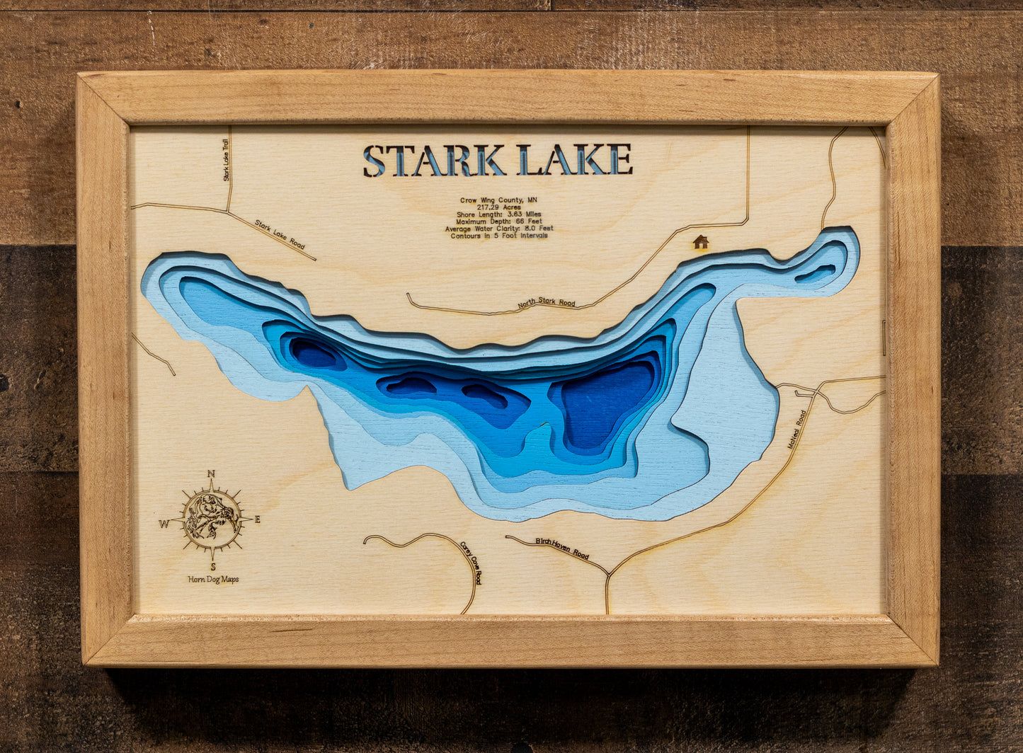 A laser-cut, layered wooden map of Stark Lake in Crow Wing County, Minnesota. The distinct shape of this natural lake, with its 3.63-mile shoreline, is clearly visible within the forested landscape of central Minnesota. The varying depths of the lake, reaching a maximum of 66 feet, are represented by different layers of wood, illustrating its impressive underwater topography.
