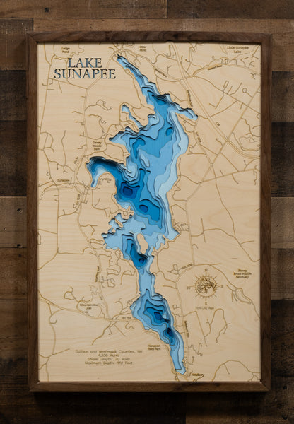 A laser-cut, layered wooden map of Lake Sunapee, located in Sullivan and Merrimack Counties, New Hampshire. The intricate shape of the lake, with its islands and varying shoreline, is clearly depicted within the western New Hampshire landscape. The varying depths of the lake, reaching a maximum of 112 feet, are represented by different layers of wood, creating a three-dimensional effect of this beautiful and popular water body.