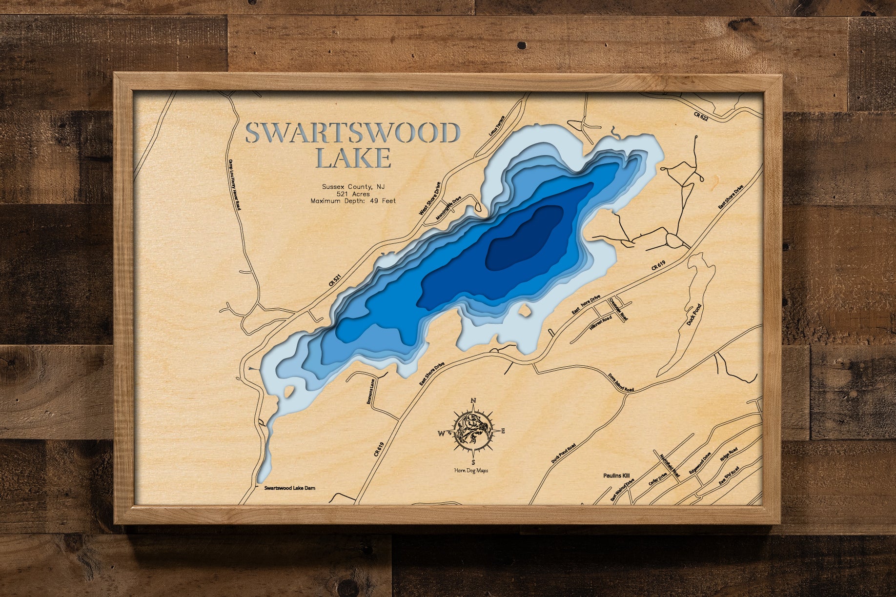A laser-cut, layered wooden map of Swartswood Lake in Sussex County, New Jersey. The distinct shape of this glacial lake, with its 7.23-mile shoreline, is clearly visible within the northern New Jersey landscape. The varying depths of the lake, reaching a maximum of 42 feet, are represented by different layers of wood, illustrating its underwater topography.