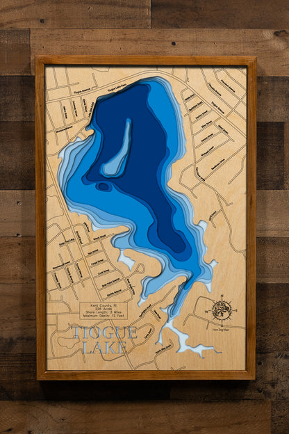 An intricately detailed, laser-cut wooden topographic map of Tiogue Lake in Kent County, Rhode Island. The layered design showcases the 226-acre reservoir's distinctive shape with its half-mile-wide open water expanse, multiple quiet bays and coves, shallow depth contours averaging six feet, and the three miles of tree-lined residential shoreline in the heart of Coventry.
