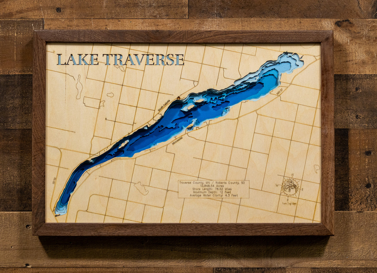 A framed wooden map plaque titled "LAKE TRAVERSE" showing the lake in layered blue tones on a light wood background, mounted on a rustic wood wall.