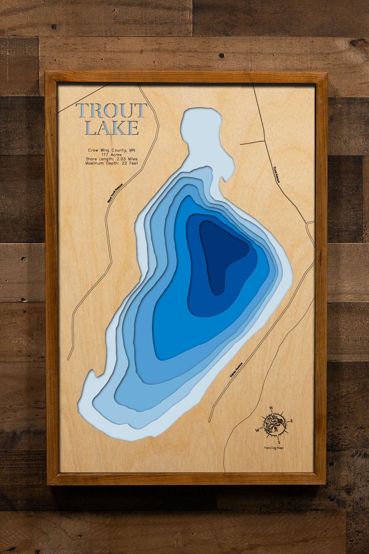 A precision laser-cut, multi-layered wooden map of Trout Lake in Crow Wing County, Minnesota, a 117-acre lake near Emily in the heart of the Brainerd Lakes region. The natural wood top layer captures just over 2 miles of intimate shoreline in fine detail, while a light-to-dark blue gradient conveys the lake's 22-foot depth. A handcrafted statement piece for any Minnesota lake cabin, home, or outdoor enthusiast's wall.