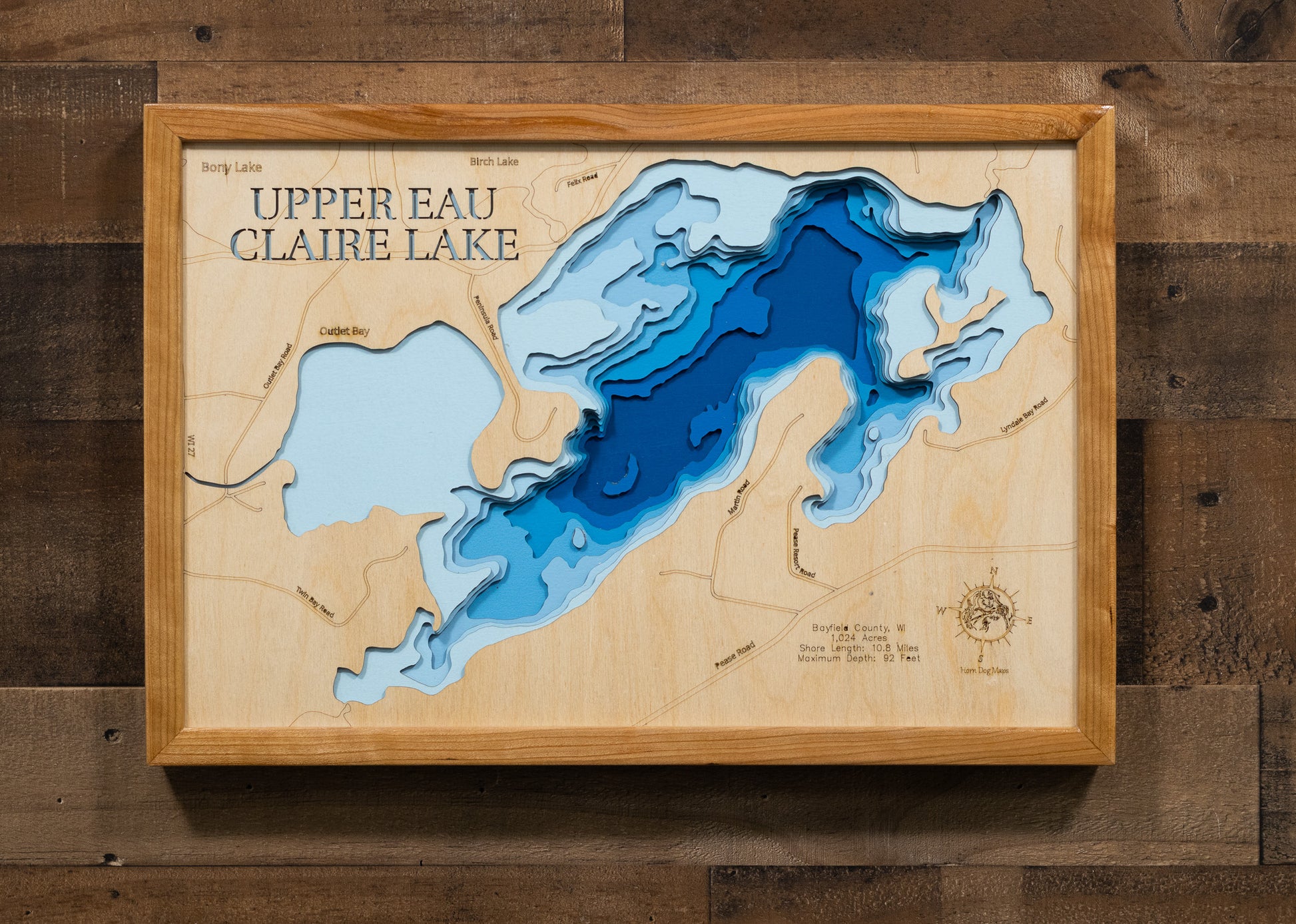 A laser-cut, layered wooden map of Upper Eau Claire Lake in Bayfield County, Wisconsin. The distinct shape of this natural lake is clearly visible within the forested landscape of northern Wisconsin. The varying depths of the lake, reaching a remarkable maximum of 92 feet, are represented by different layers of wood, illustrating its impressive underwater topography.
