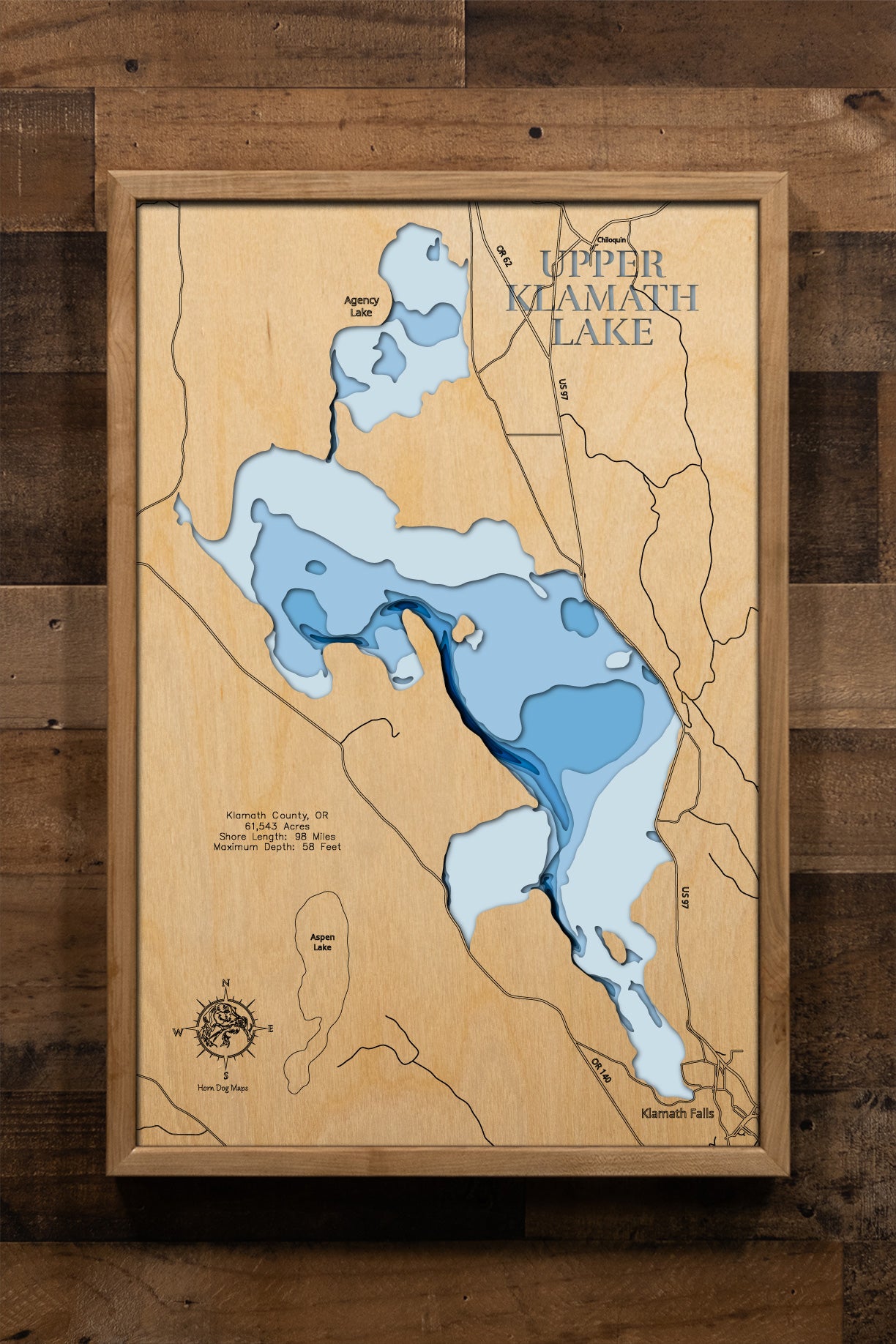 A meticulously crafted, multi-layered wooden topographic map of Upper Klamath Lake in Klamath County, Oregon. The laser-cut design showcases the lake's impressive 61,543-acre expanse stretching nearly 25 miles, the distinctive narrow western trench reaching 58-foot depths, the extensive marshlands and bays including Pelican Bay, and the 98 miles of intricate shoreline detail.