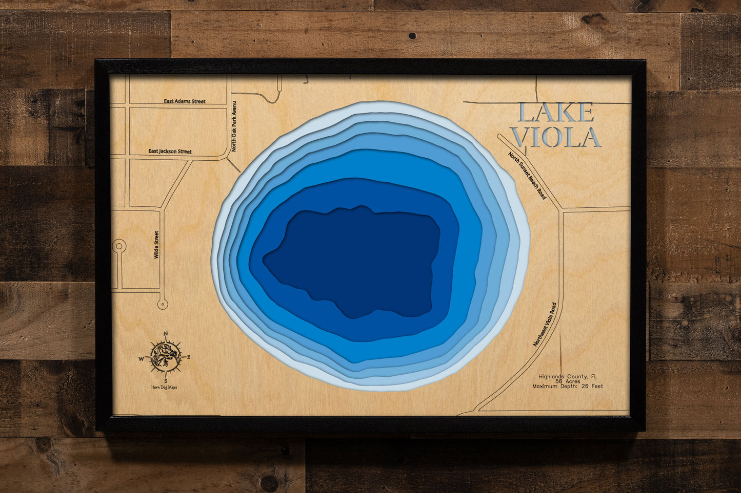 A precision laser-cut, multi-layered wooden map of Lake Viola in Highlands County, Florida — a 56-acre round natural lake directly north of Avon Park with a maximum depth of 26 feet. The natural wood top layer captures the lake's nearly circular shoreline in fine detail, while a light-to-dark blue gradient conveys its clear, spring-influenced character. A handcrafted statement piece for any Florida lake home, cabin, or outdoor enthusiast's wall.