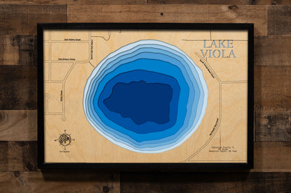 A precision laser-cut, multi-layered wooden map of Lake Viola in Highlands County, Florida — a 56-acre round natural lake directly north of Avon Park with a maximum depth of 26 feet. The natural wood top layer captures the lake's nearly circular shoreline in fine detail, while a light-to-dark blue gradient conveys its clear, spring-influenced character. A handcrafted statement piece for any Florida lake home, cabin, or outdoor enthusiast's wall.