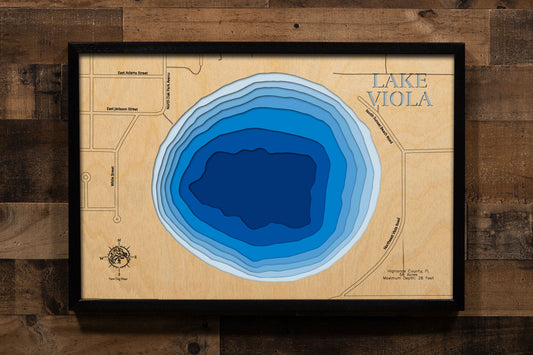A precision laser-cut, multi-layered wooden map of Lake Viola in Highlands County, Florida — a 56-acre round natural lake directly north of Avon Park with a maximum depth of 26 feet. The natural wood top layer captures the lake's nearly circular shoreline in fine detail, while a light-to-dark blue gradient conveys its clear, spring-influenced character. A handcrafted statement piece for any Florida lake home, cabin, or outdoor enthusiast's wall.