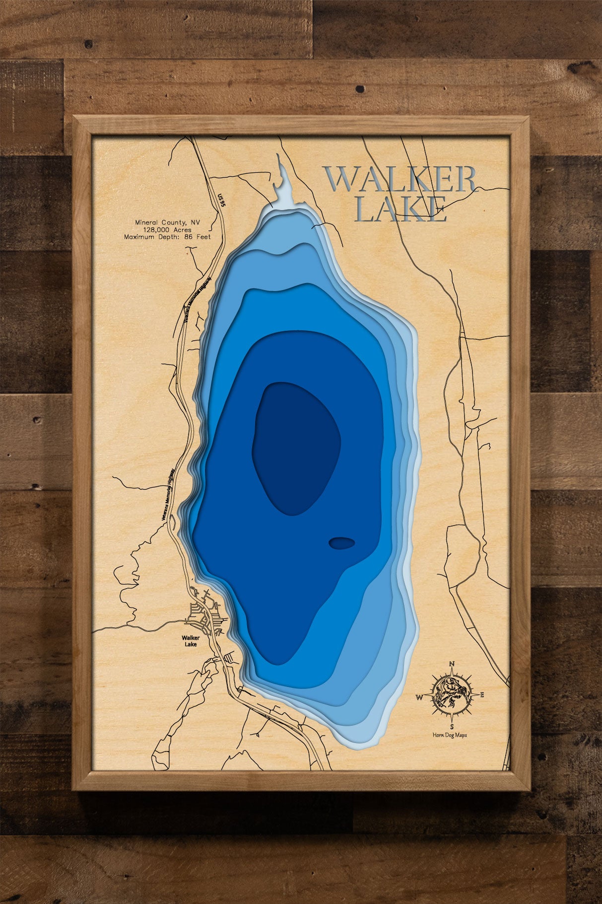 A laser-cut, layered wooden map of Walker Lake in Mineral County, Nevada. The shape of the lake, dramatically reduced from its historical size, is visible within the Nevada desert landscape. The varying depths of the lake are represented by different layers of wood, illustrating the significant changes in its water levels over time.