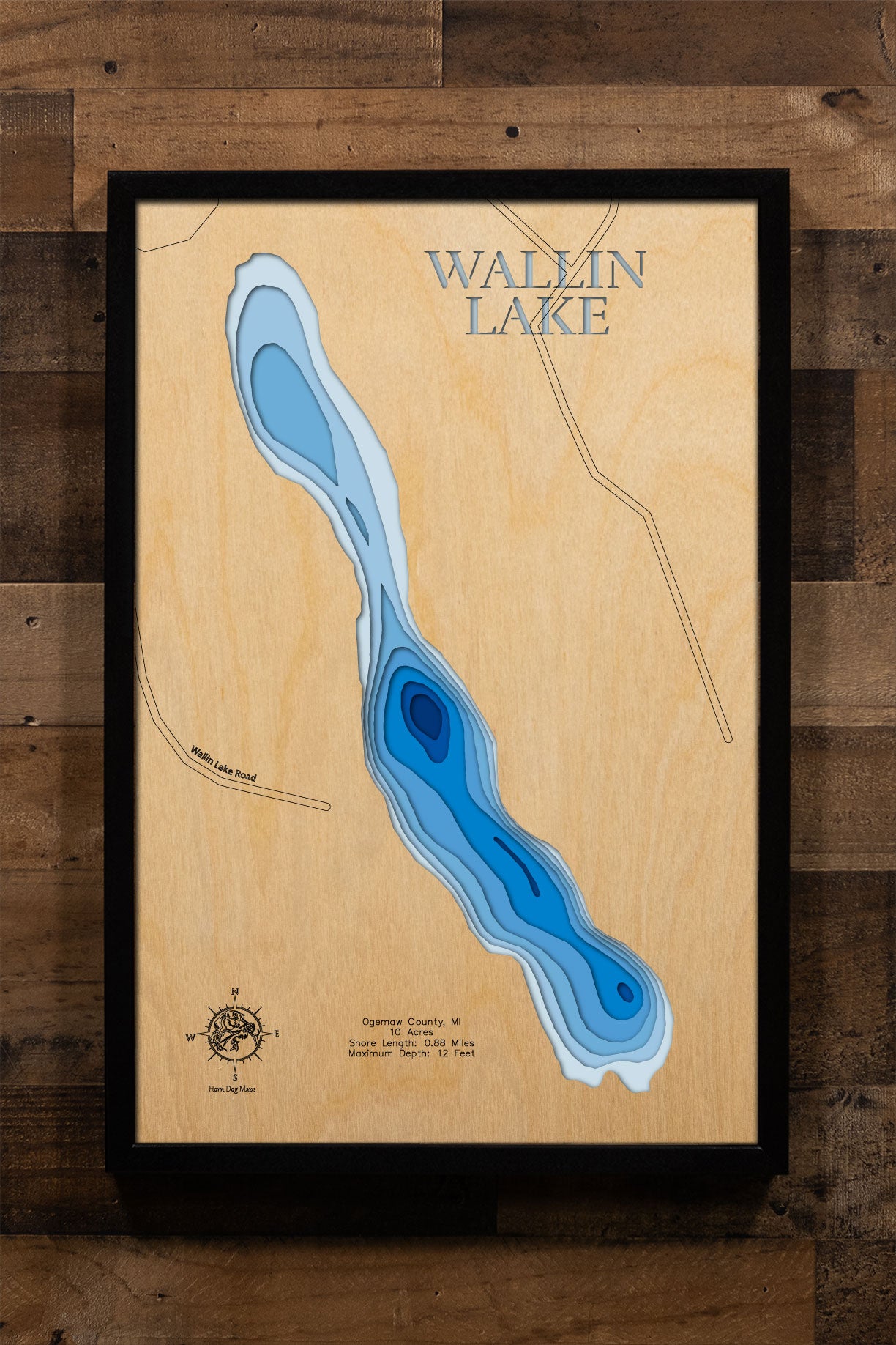 A precision laser-cut, multi-layered wooden map of Wallin Lake in Ogemaw County, Michigan — a small, secluded 10-acre lake in Klacking Township near West Branch in northern Michigan's Au Sable River country. The natural wood top layer captures its intimate shoreline in fine detail, while a light-to-dark blue gradient conveys the lake's 12-foot depth. A handcrafted statement piece for any Michigan lake cabin, home, or outdoor enthusiast's wall.