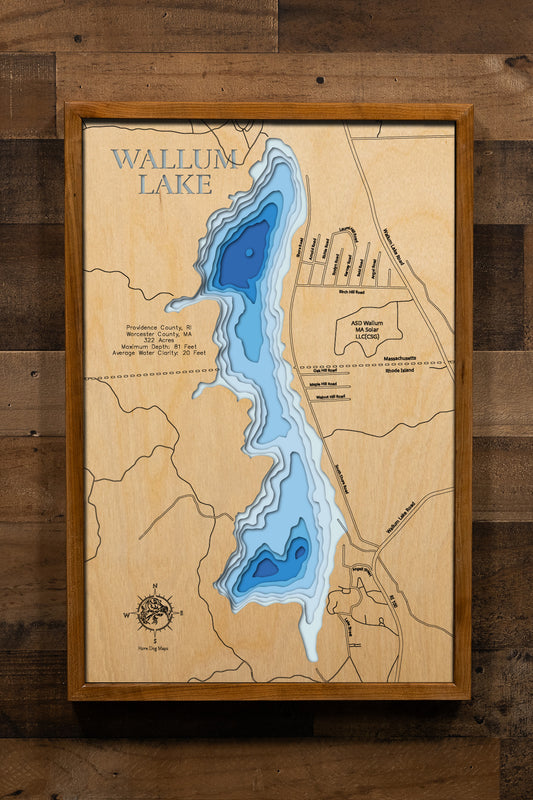 A meticulously crafted, multi-layered wooden topographic map of Wallum Lake straddling the Rhode Island-Massachusetts border in Providence and Worcester Counties. The laser-cut artwork reveals intricate depth contours descending from shallow shores to the 81-foot maximum depth, the lake's nearly two-mile elongated shape, and the distinctive state boundary line bisecting the waterbody, with protected Douglas State Forest lands along the western shore.