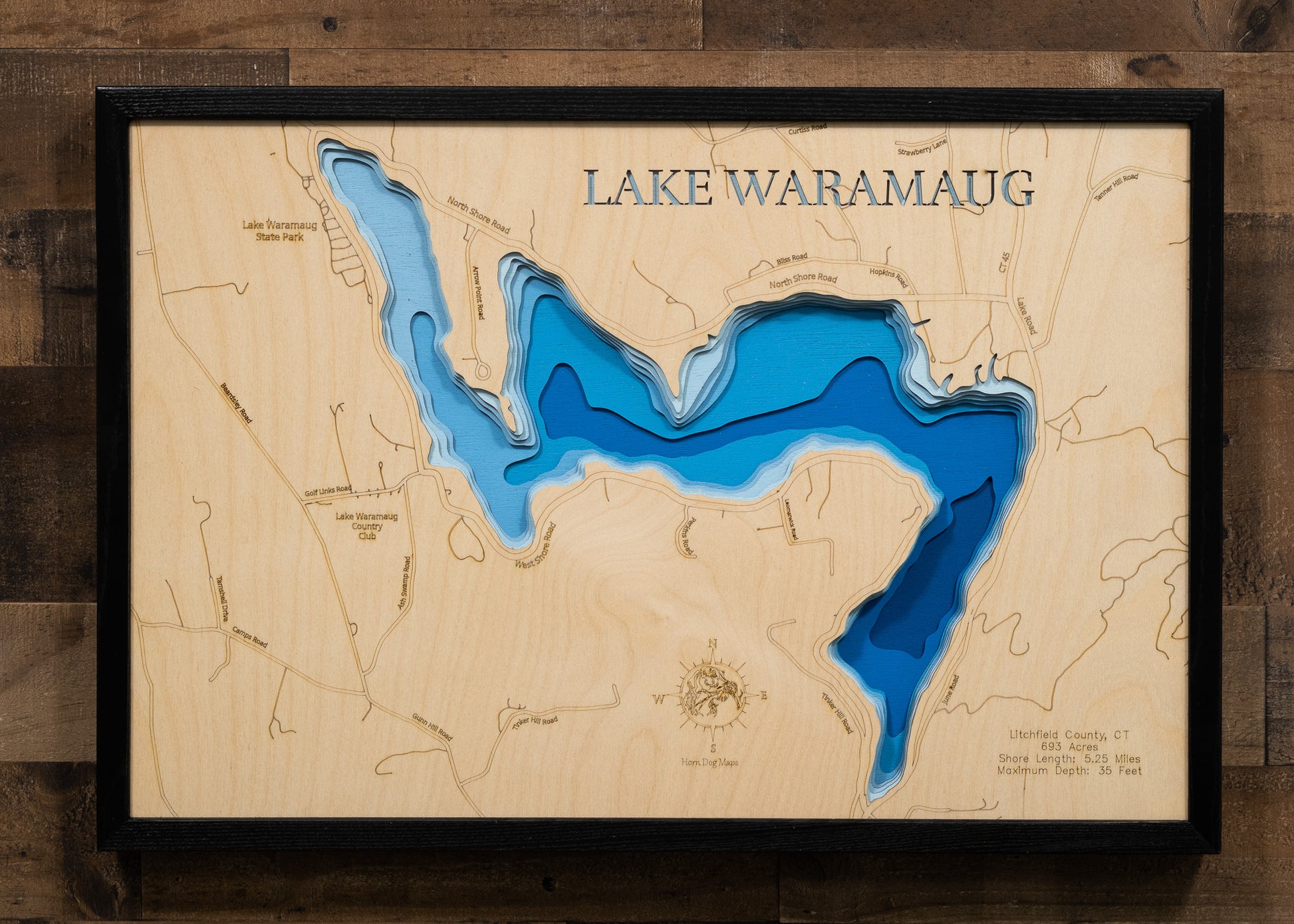 A laser-cut, layered wood map of Lake Waramaug, Connecticut, illustrating its winding shoreline and forested surroundings in Litchfield County.