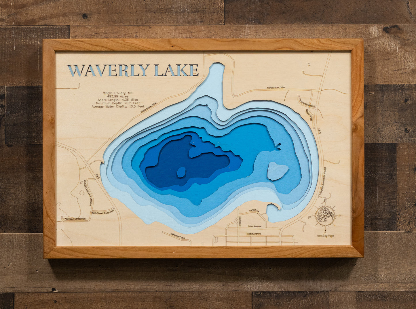 A laser-cut, layered wooden map of Waverly Lake in Wright County, Minnesota. The distinct shape of this natural lake is clearly visible within the forested landscape of central Minnesota. The varying depths of the lake, reaching a maximum of 70.5 feet, are represented by different layers of wood, illustrating its impressive underwater topography.