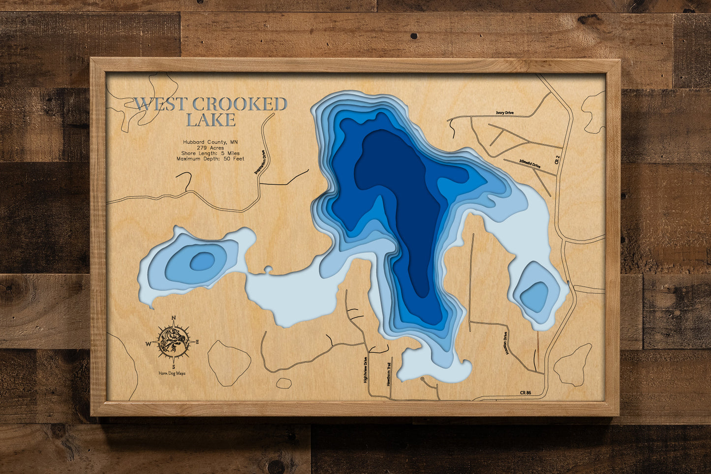 A detailed, laser-cut, multi-layered wooden map of West Crooked Lake in Hubbard County, Minnesota, showcasing the 279-acre Class 25 lake with 5 miles of irregular shoreline nestled in the Paul Bunyan State Forest near Nevis. The topographic design features natural wood layers highlighting the towering pines and graduated blue water layers illustrating depths to the 50-foot maximum.
