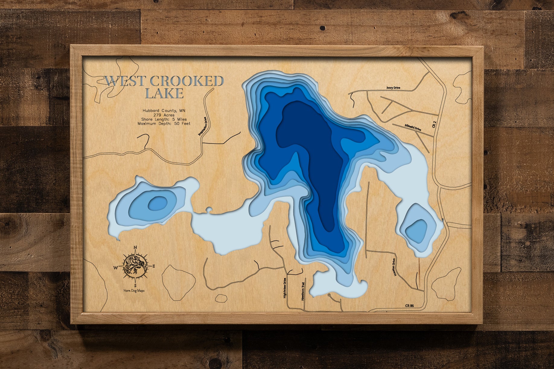 A detailed, laser-cut, multi-layered wooden map of West Crooked Lake in Hubbard County, Minnesota, showcasing the 279-acre Class 25 lake with 5 miles of irregular shoreline nestled in the Paul Bunyan State Forest near Nevis. The topographic design features natural wood layers highlighting the towering pines and graduated blue water layers illustrating depths to the 50-foot maximum.