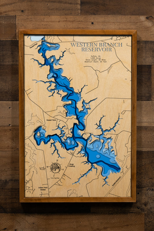 A magnificently detailed, laser-cut, multi-layered wooden topographical map of Western Branch Reservoir in Suffolk, Virginia, showcasing the 1,265-acre horseshoe-shaped water supply reservoir with 40 miles of irregular shoreline and connections to Lake Prince and Burnt Mills. The natural wood top layer frames two public boat launches, the dam on the western branch of Nansemond River, and sunken island hot spots, while graduated blue layers create a stunning visual gradient from shallow areas to the 35-foot 