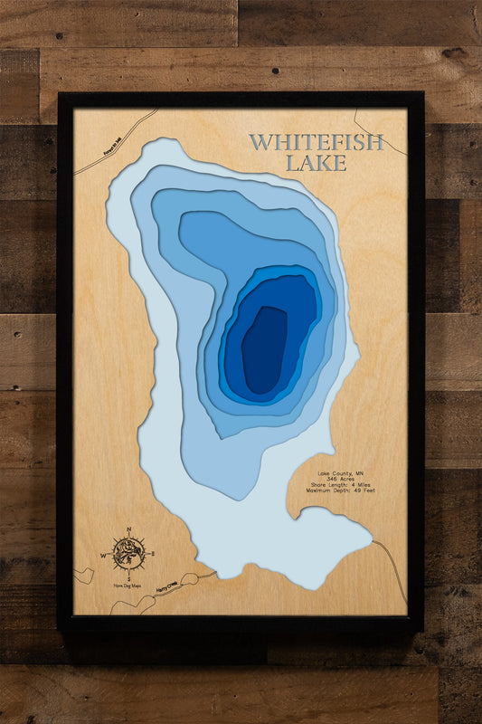 A detailed, laser-cut, multi-layered wooden map of Whitefish Lake in Lake County, Minnesota, showcasing the lake's 346-acre surface area with 4 miles of intricate shoreline detail. The topographic representation displays depth contours from shallow areas to the 49-foot maximum depth, with natural wood upper layers highlighting the surrounding Superior National Forest terrain and graduated blue water layers.