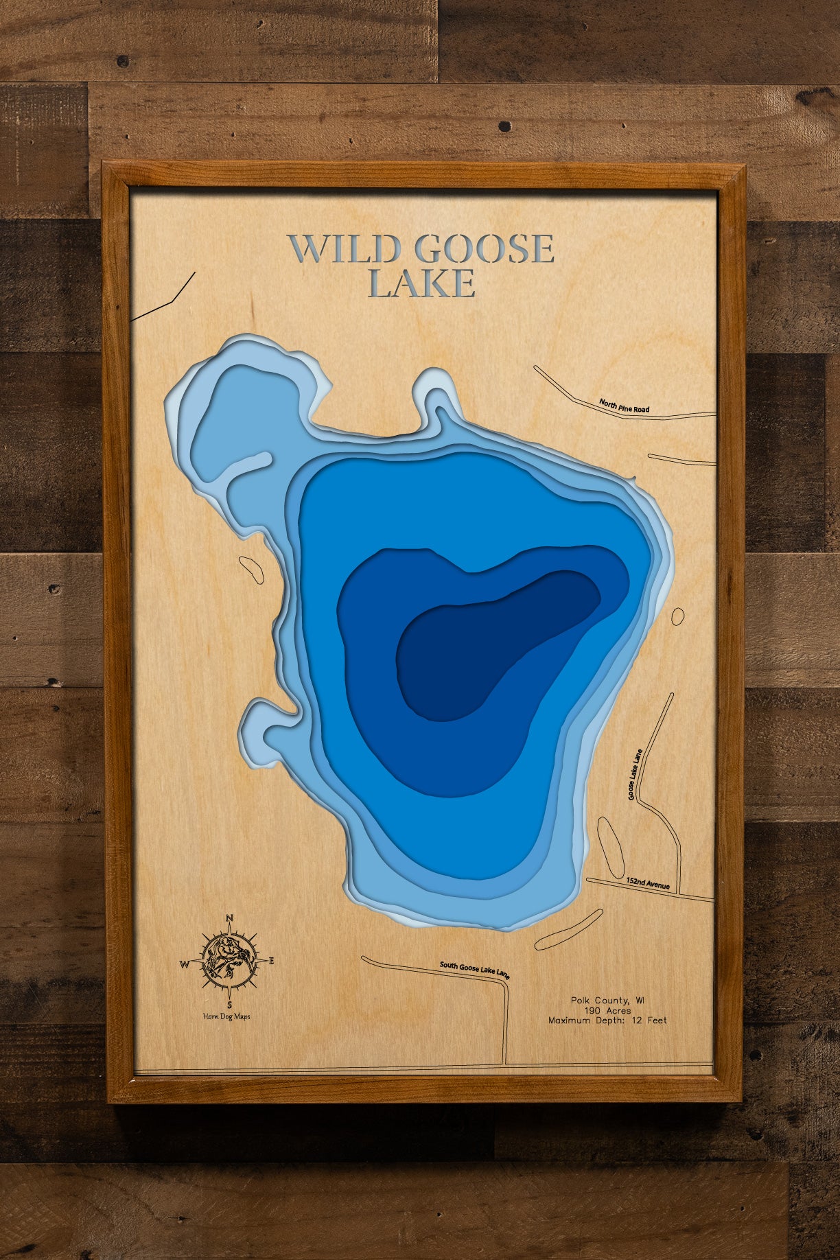 A precision laser-cut, multi-layered wooden map of Wild Goose Lake in Polk County, Wisconsin. The natural wood top layer captures the lake's wooded, organic shoreline in fine detail, while a light-to-dark blue gradient highlights the water's depth and dimension. A distinctive, rustic statement piece crafted for cabin walls, fishing lodges, or any Wisconsin lake-inspired living space.