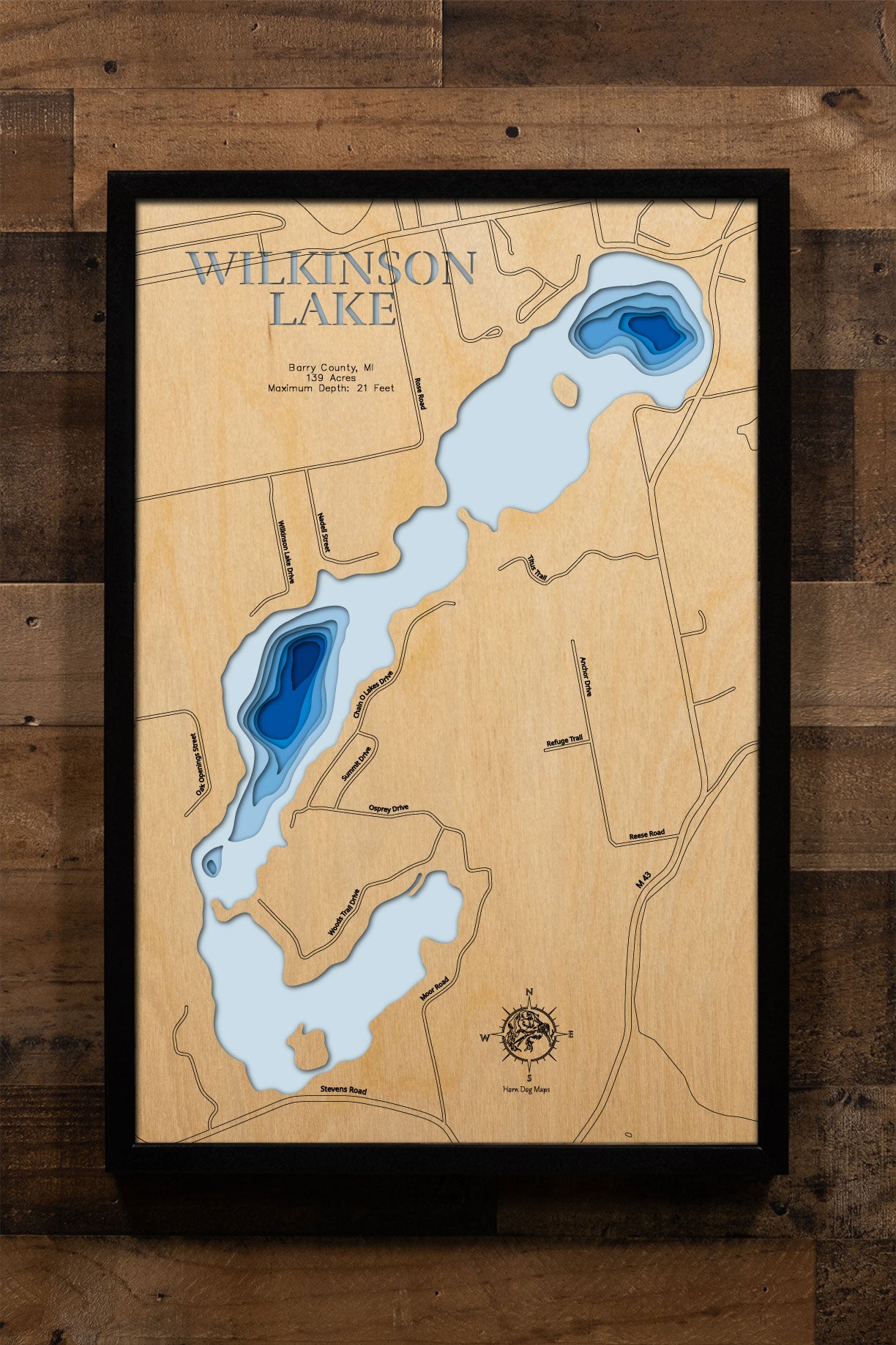 A precision laser-cut, multi-layered wooden map of Wilkinson, Jones, and Cloverdale Lakes in Barry County, Michigan, the connected Chain O' Lakes near Delton in southwest Michigan's lake country. The natural wood top layer traces all three lakes' shorelines in fine detail, while a light-to-dark blue gradient conveys depths ranging from 21 to 50 feet across the chain. A handcrafted statement piece for any Michigan lake home, cabin, or outdoor enthusiast's wall.