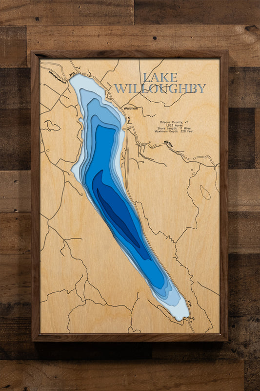 A magnificently detailed, laser-cut, multi-layered wooden topographical map of Lake Willoughby in Orleans County, Vermont, showcasing the dramatic 1,653-acre glacial lake stretching five miles between the fjord-like cliffs of Mount Pisgah and Mount Hor with depth contours plunging to the astounding 328-foot maximum depth. The natural wood top layer frames 11 miles of shoreline including the iconic Willoughby Gap, two public beaches, and the Willoughby State Forest, while graduated blue layers create a stunn