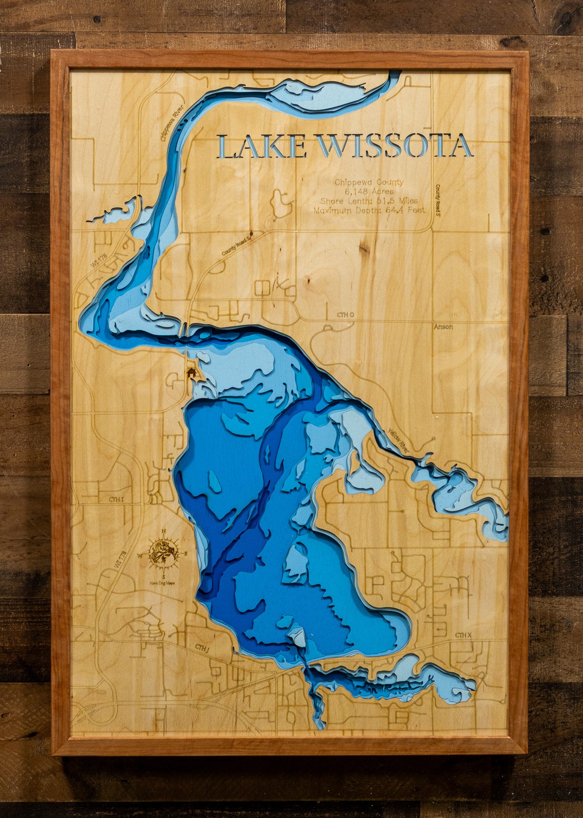 A framed wooden map of Lake Wissota, featuring layered blue resin depths and engraved wood details, mounted on a dark wood plank wall.