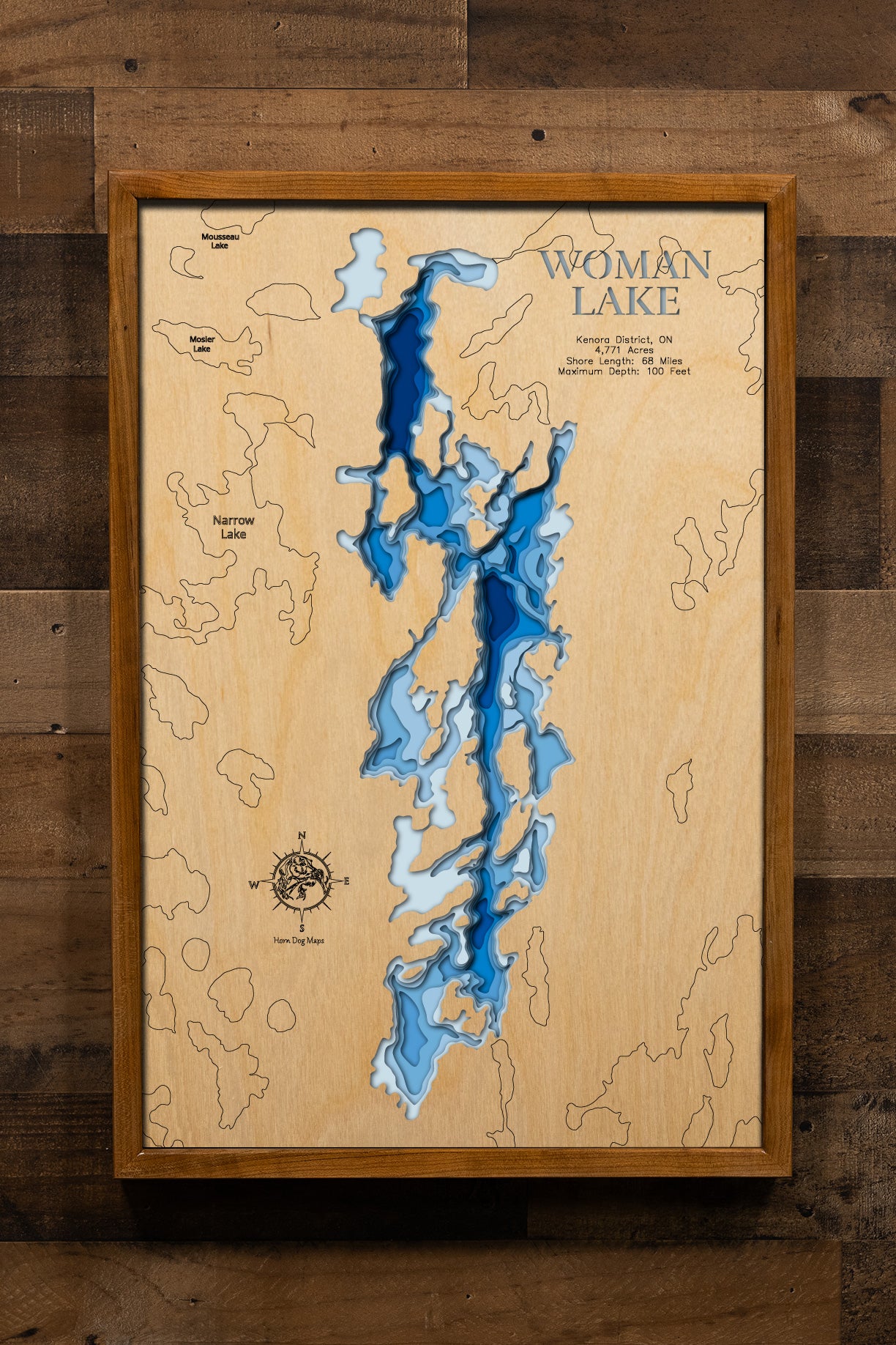 A magnificently detailed, laser-cut, multi-layered wooden topographical map of Woman Lake in Kenora District, Ontario, showcasing the expansive 4,771-acre wilderness lake with an incredible 68 miles of irregular rocky shoreline. The natural wood top layer frames the Woman River inlet, countless hidden bays and rocky points, and connections to the Woman River chain of lakes, while graduated blue layers create a stunning visual gradient from shallow rocky areas to the impressive 100-foot maximum depth.