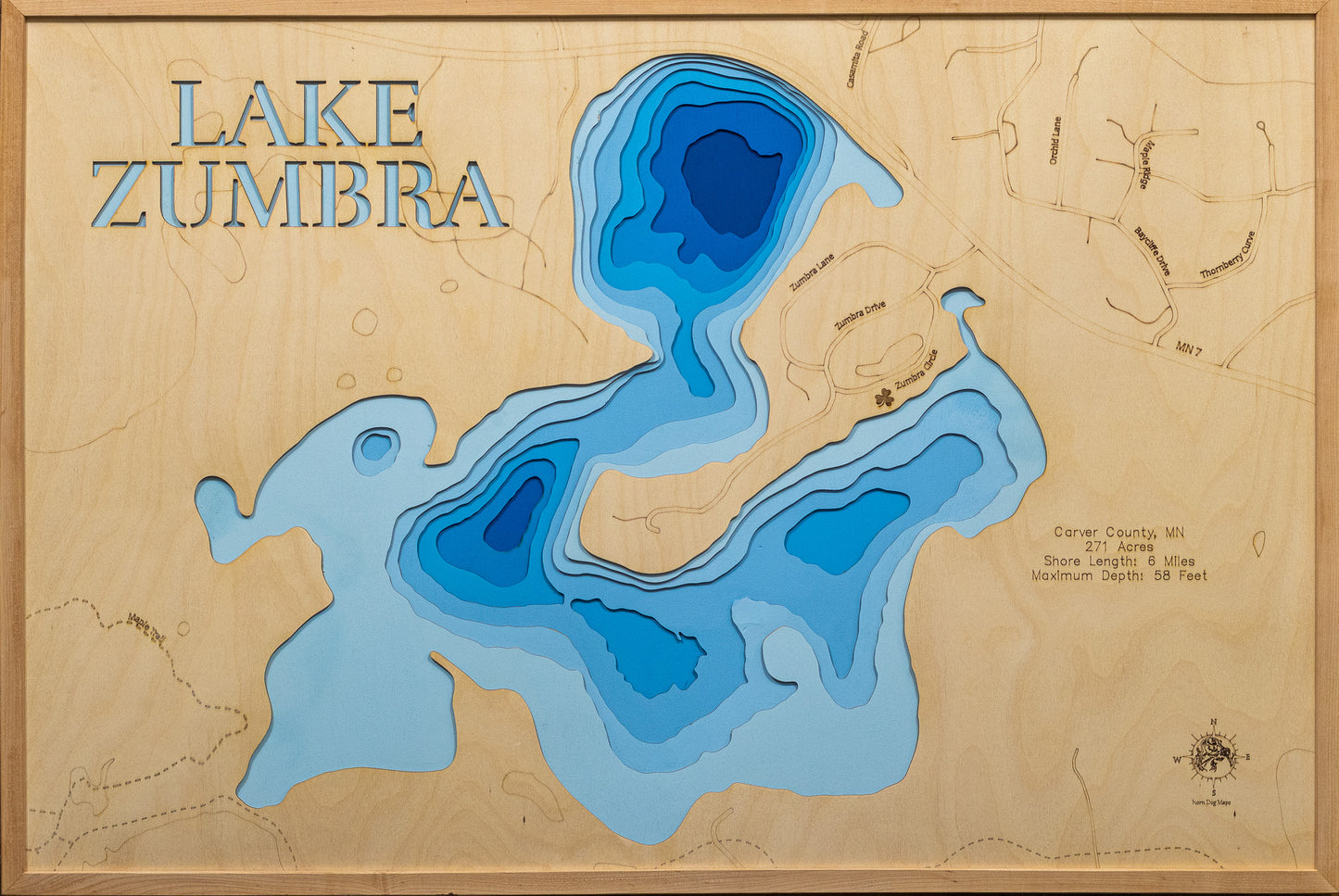 A meticulously detailed, laser-cut, multi-layered wooden topographical map of Lake Zumbra in Carver County, Minnesota, showcasing the 271-acre lake within Carver Park Reserve with depth contours from the 14-foot average to the 58-foot maximum depth. The natural wood top layer frames six miles of mostly undeveloped shoreline protected by Three Rivers Park District near Victoria, while graduated blue layers create a striking visual depth gradient across this premier Northern Pike fishery.