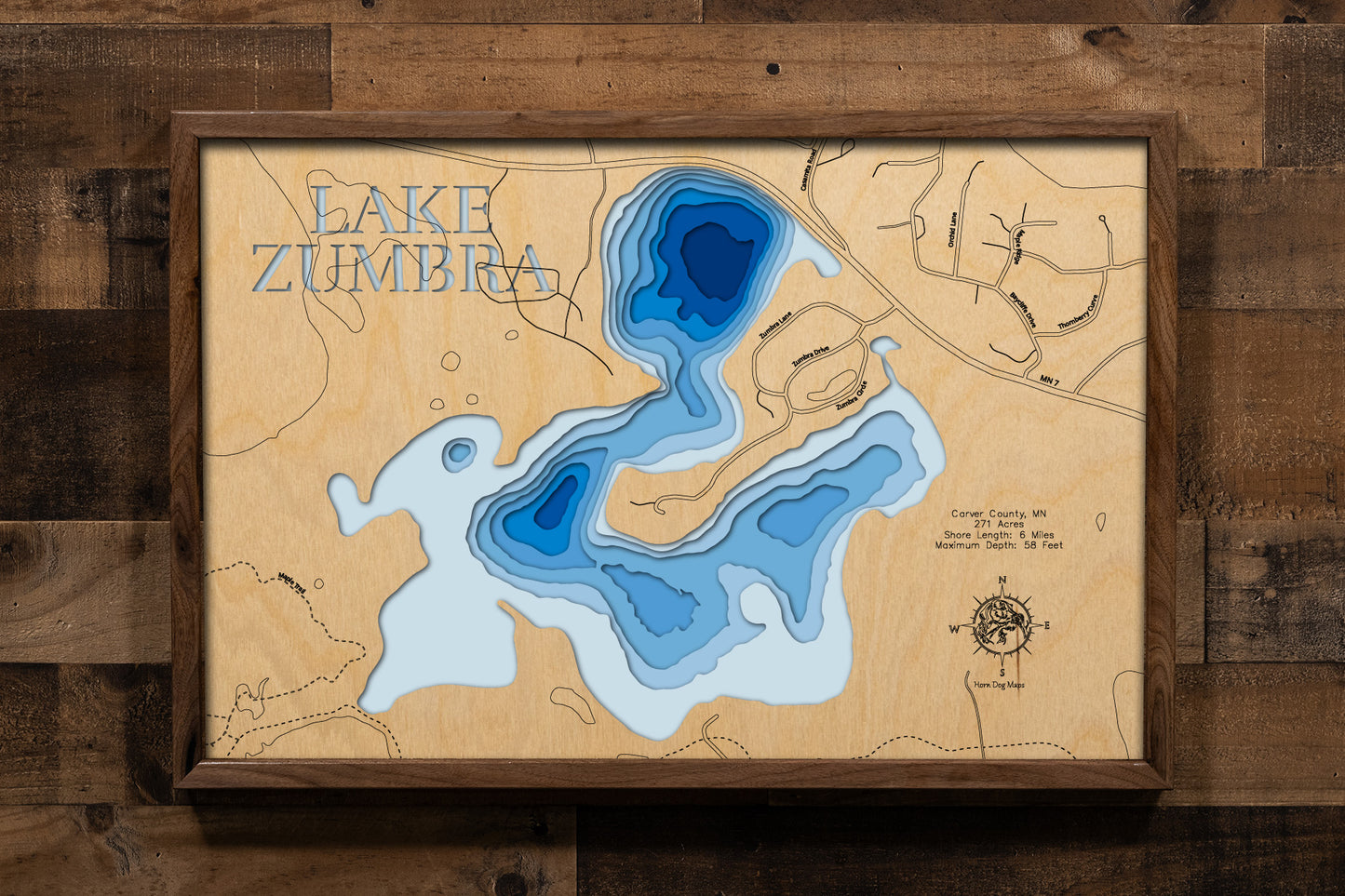 A meticulously detailed, laser-cut, multi-layered wooden topographical map of Lake Zumbra in Carver County, Minnesota, showcasing the 271-acre lake within Carver Park Reserve with depth contours from the 14-foot average to the 58-foot maximum depth. The natural wood top layer frames six miles of mostly undeveloped shoreline protected by Three Rivers Park District near Victoria, while graduated blue layers create a striking visual depth gradient across this premier Northern Pike fishery.
