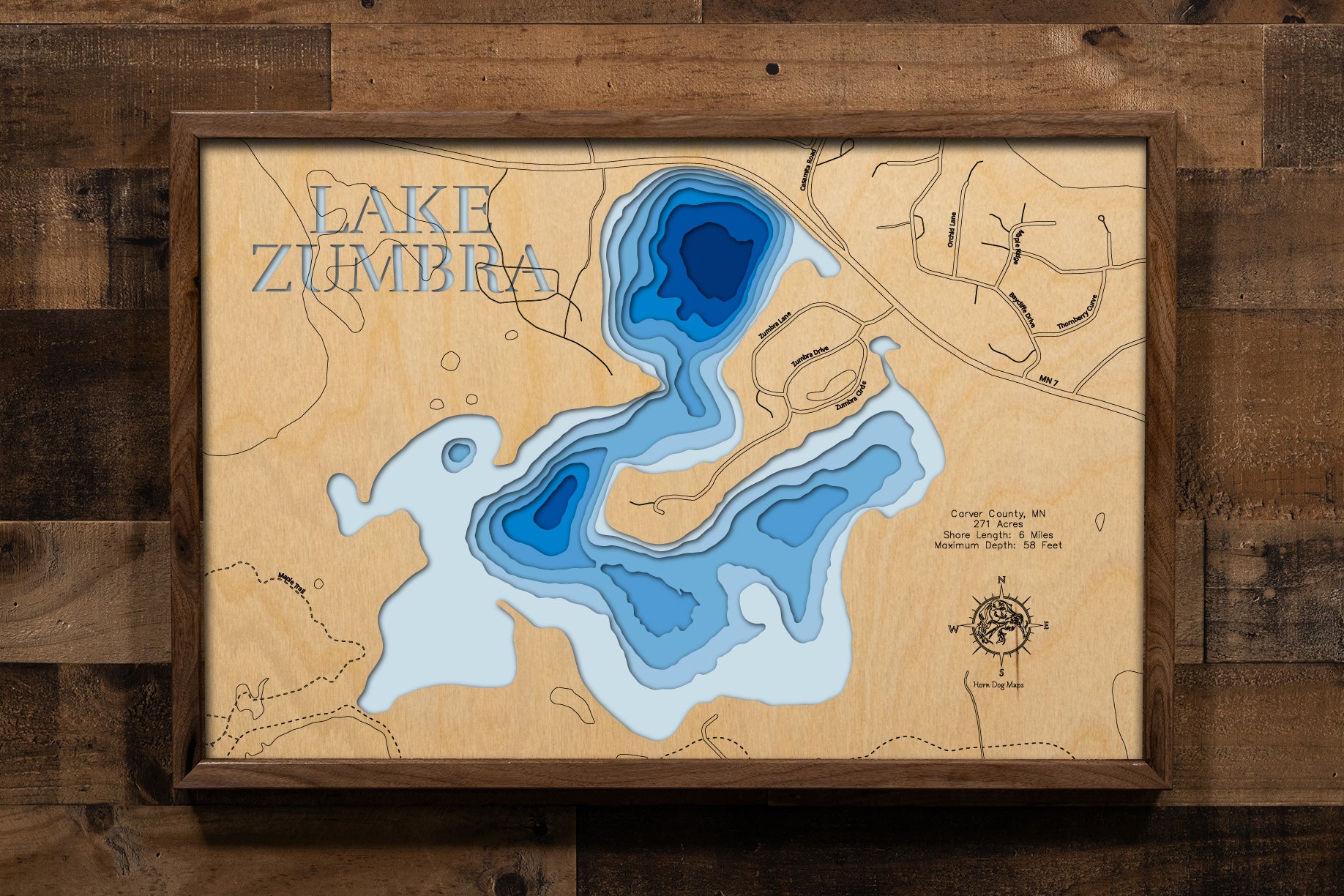 A meticulously detailed, laser-cut, multi-layered wooden topographical map of Lake Zumbra in Carver County, Minnesota, showcasing the 271-acre lake within Carver Park Reserve with depth contours from the 14-foot average to the 58-foot maximum depth. The natural wood top layer frames six miles of mostly undeveloped shoreline protected by Three Rivers Park District near Victoria, while graduated blue layers create a striking visual depth gradient across this premier Northern Pike fishery.