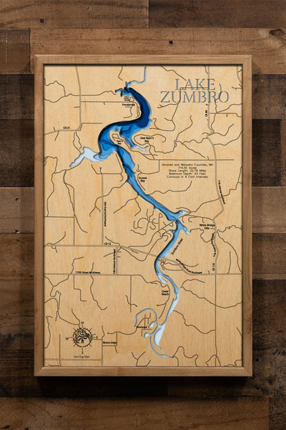 A laser-cut, layered wooden map of Lake Zumbro in Olmsted and Wabasha Counties, Minnesota. The distinct, elongated shape of this reservoir, with its 22.78-mile shoreline, is clearly visible as it winds through the bluffs of southeastern Minnesota. The varying depths of the lake, reaching a maximum of 43 feet and detailed by 6-foot contour intervals, are represented by different layers of wood, illustrating its impressive underwater topography.