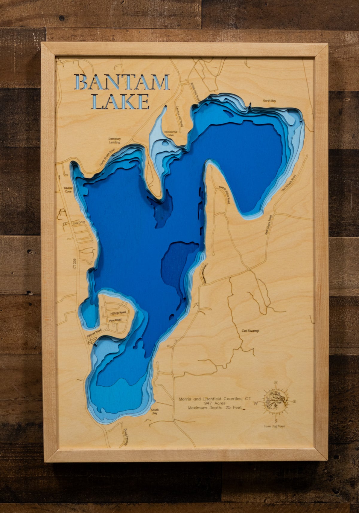 A laser-cut, layered wooden map of Bantam Lake, located in Morris and Litchfield Counties, Connecticut. The shape of Connecticut's largest natural lake is clearly defined within the northwestern Connecticut landscape. The varying depths of the lake, reaching a maximum of 25 feet, are represented by different layers of wood.