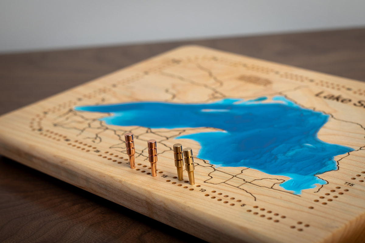 Horn Dog Maps custom maple cribbage board showing heavy metal peg options in copper and brass with blue epoxy lake fill on Lake Superior design